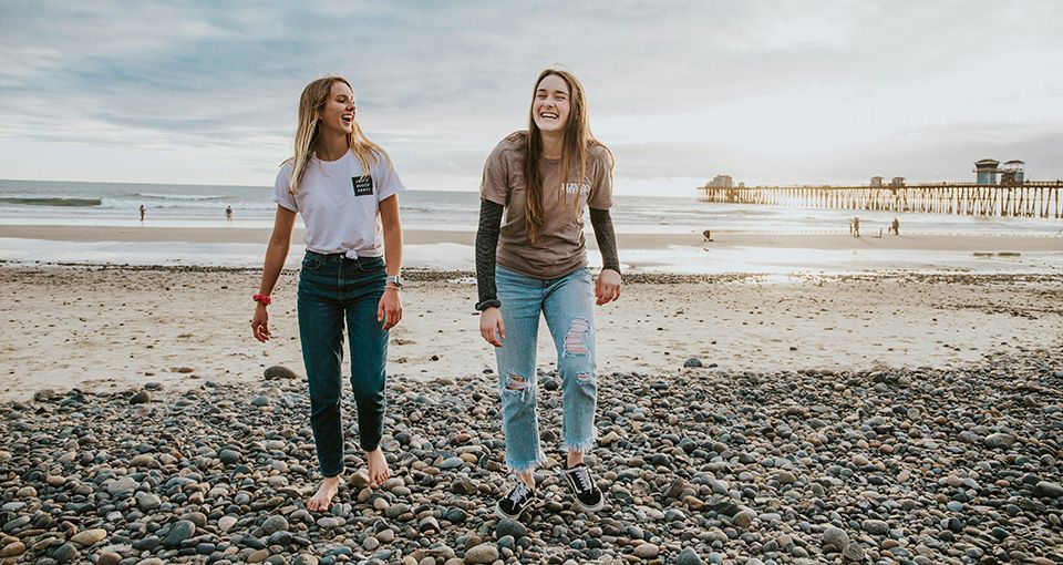 2 junge Frauen, fröhlich lachend an einem Strand